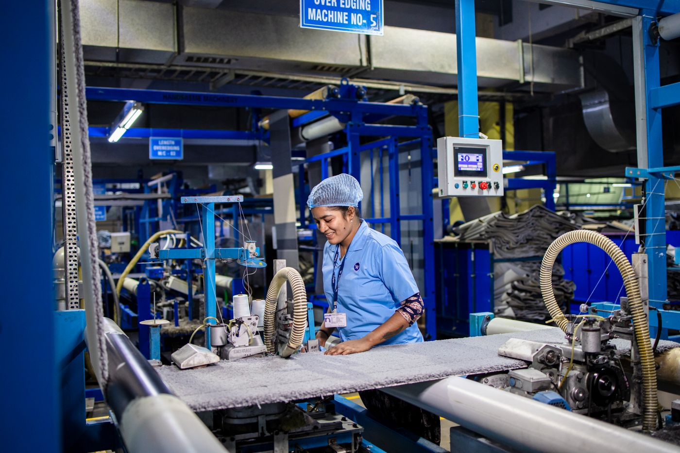 A worker in a hair cap operating machinery on a blue production line in an Indian factory